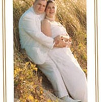 Couple in white attire on a grassy hill.